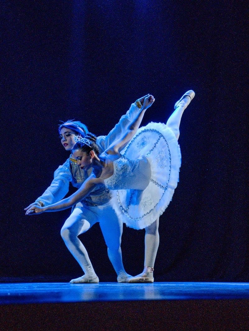 Un pas de deux de alumnas avanzadas en una función, bajo luz azul